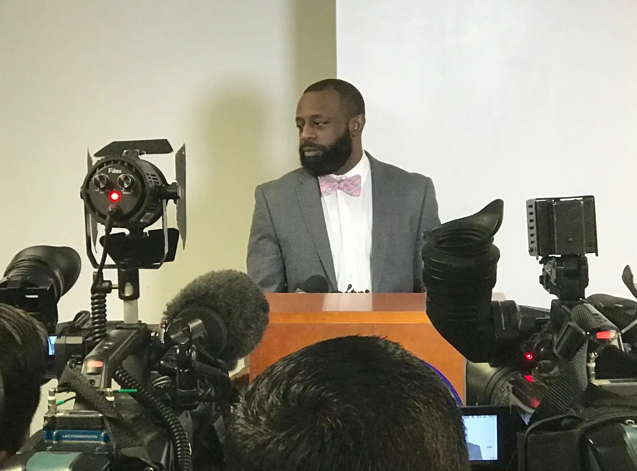 A man in a suit and bow tie is speaking to the press.