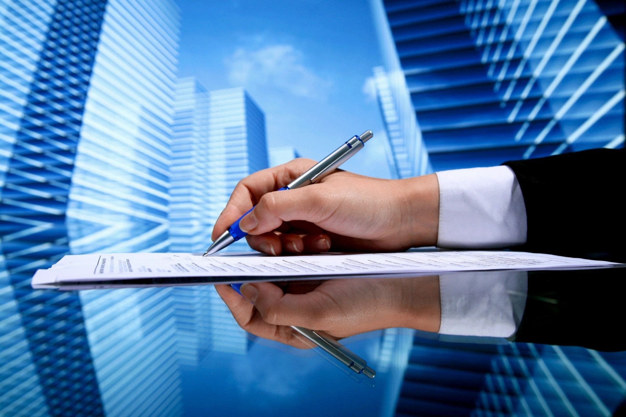 A person writing on paper with buildings in the background.